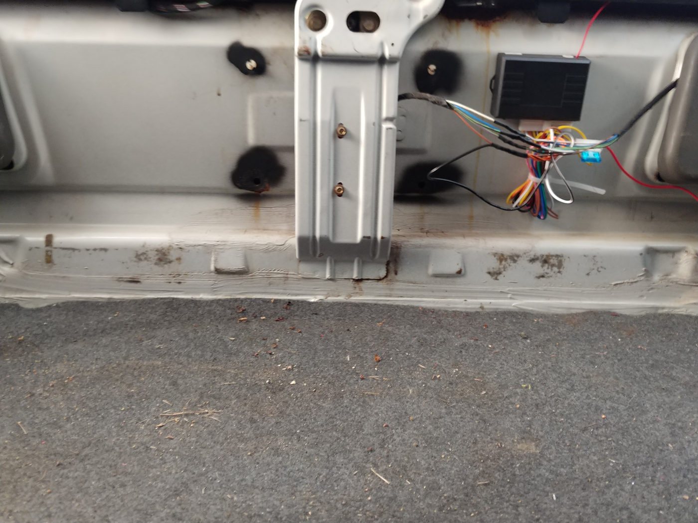 The remote lock control unit stuck to the boot wall beside the wiring, with the red 12 volt wire running to it