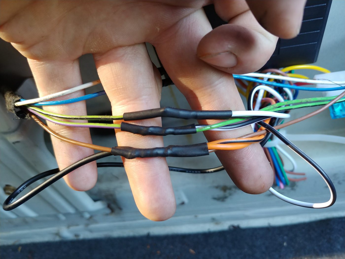 Three finished solder joints covered in black heat-shrink, joining the lock kit wires to the car wires